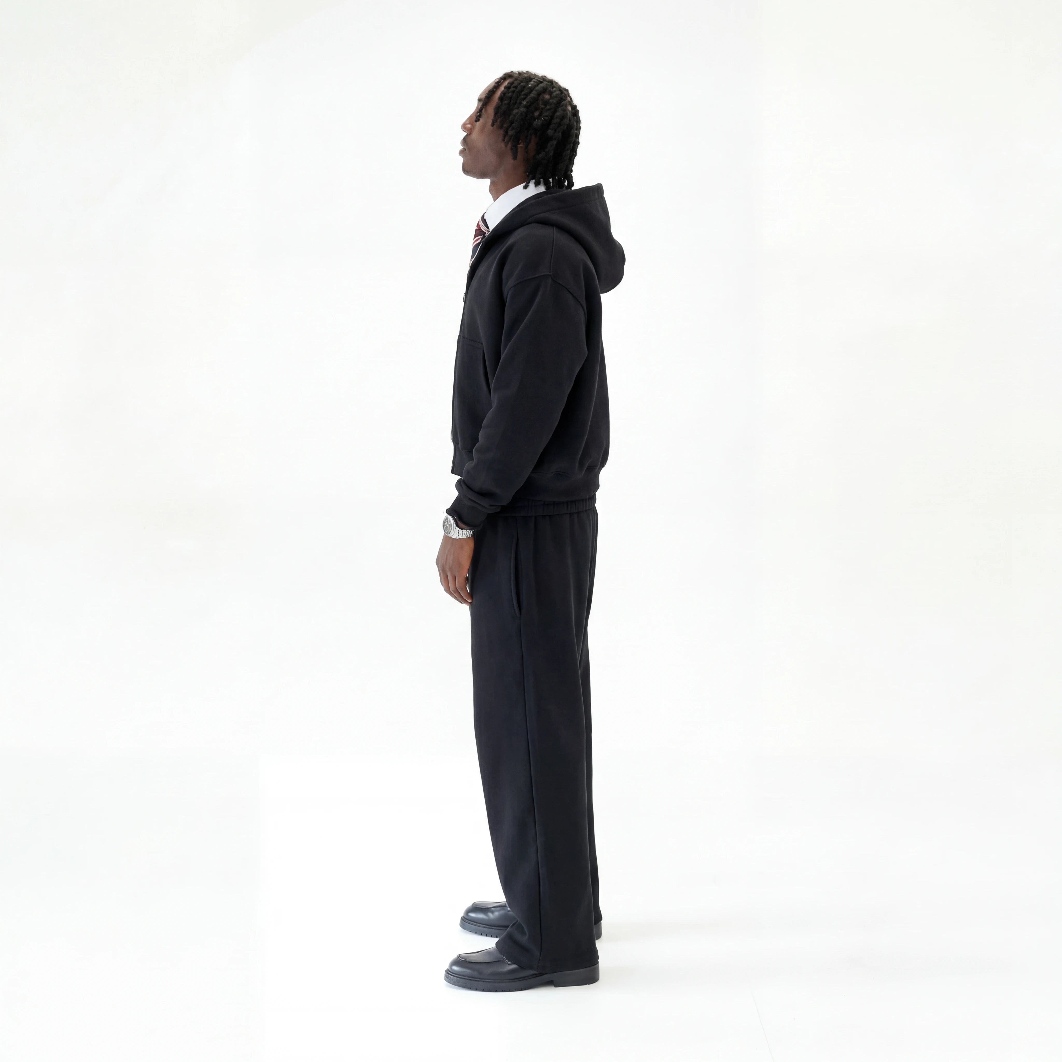 Model wearing Premium black tracksuit on white studio background facing the side.